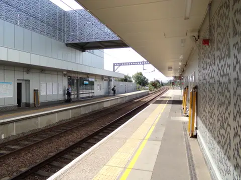 An empty platform at Cambridge North station with a modern patterned canopy and overhead electric wires