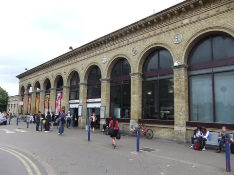 The long arched yellow brick front of Cambridge railway station with people walking past