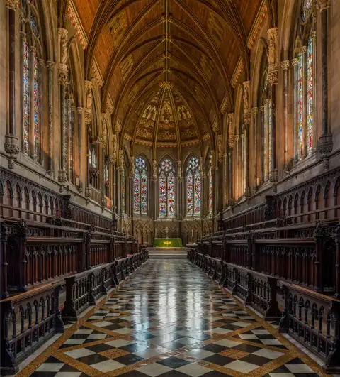 Interior of St John's College Chapel in Cambridge, with carved wooden choir stalls facing each other across a tiled floor